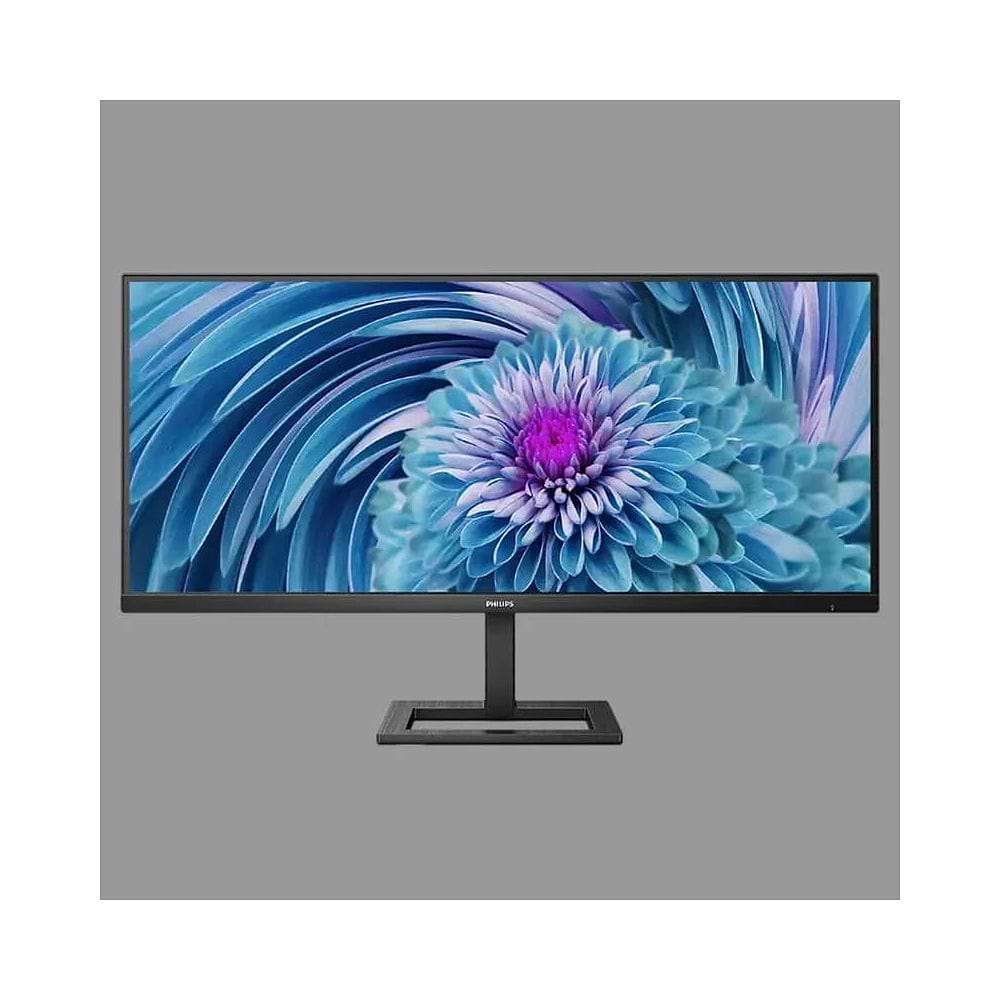צג מחשב Philips UltraWide בעיצוב מודרני בצבע שחור, עם מסך רחב במיוחד בפורמט פנורמי ומסגרת דקה. הצג מותקן על מעמד מרכזי מלבני בעל בסיס פתוח ויציב. על המסך מוצגת תמונה צבעונית של פרח בגווני כחול, טורקיז וסגול, המדגישה את שטח התצוגה הרחב ואת המראה האלגנטי של