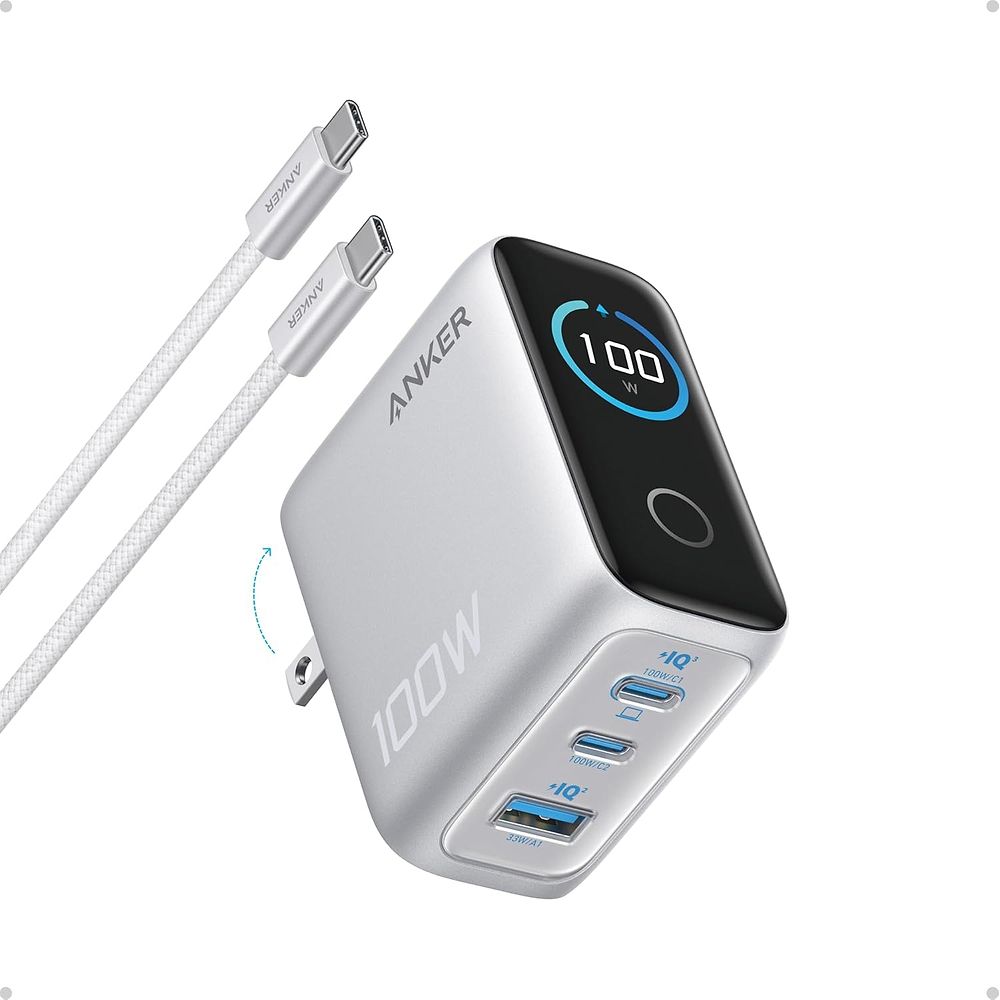 תמונה של מטען Anker 100W עם תצוגה חכמה בצבע כסוף. בחזית המטען מופיע מסך דיגיטלי המציג את עוצמת הטעינה בזמן אמת (100W). המטען כולל 3 יציאות טעינה – שתי יציאות USB-C ויציאת USB-A, ולצדו מוצג כבל USB-C ל-USB-C בצבע לבן. העיצוב קומפקטי עם תקע מתקפל לנשיאה נוח